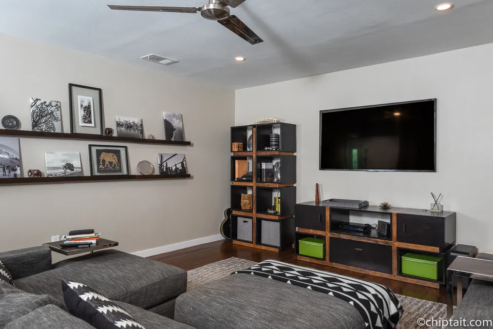 Media room with a grey sectional, floating shelves and a TV