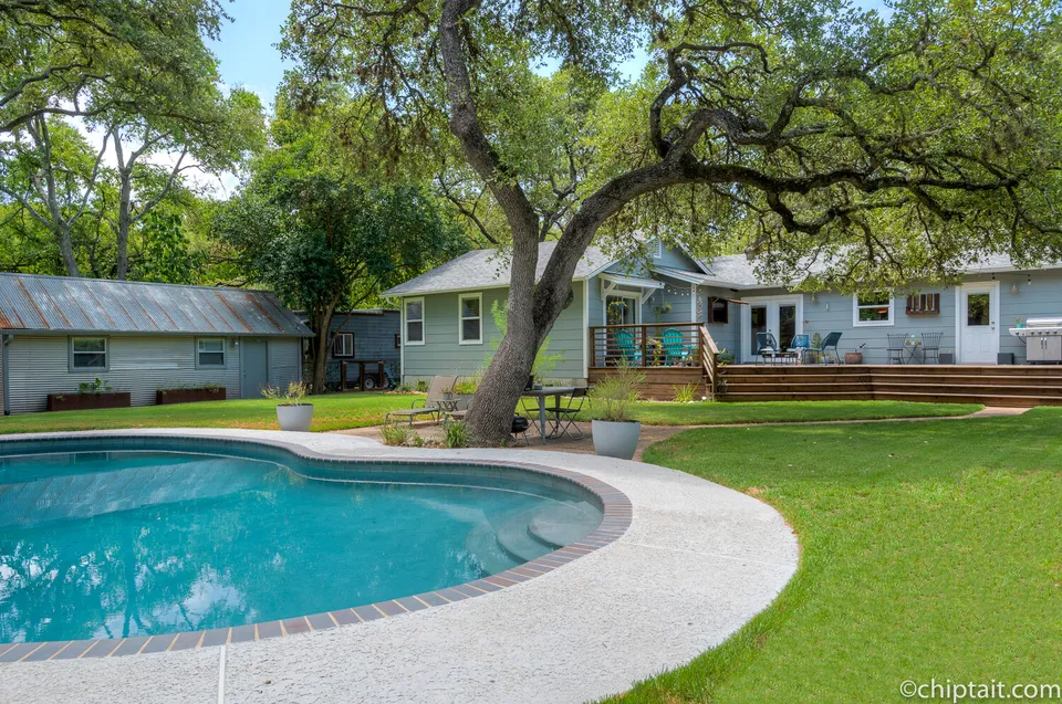 Pool with brick coping and the back of the house under oak trees
