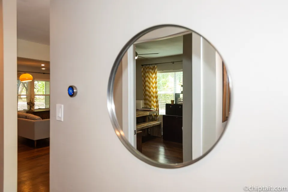 Round mirror in a hallway reflecting the living room