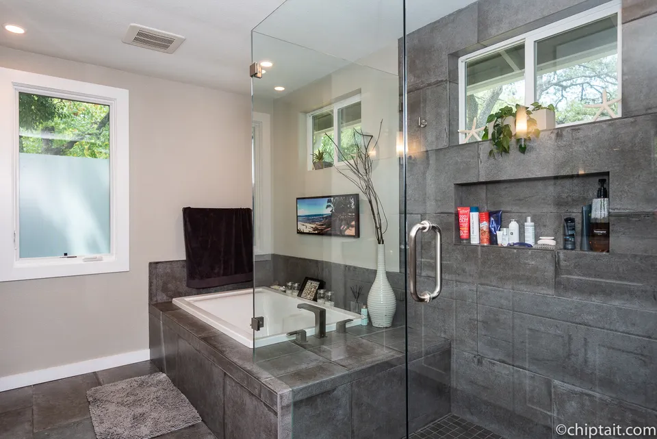 Soaking tub and glass shower with dark slate tile and a niche