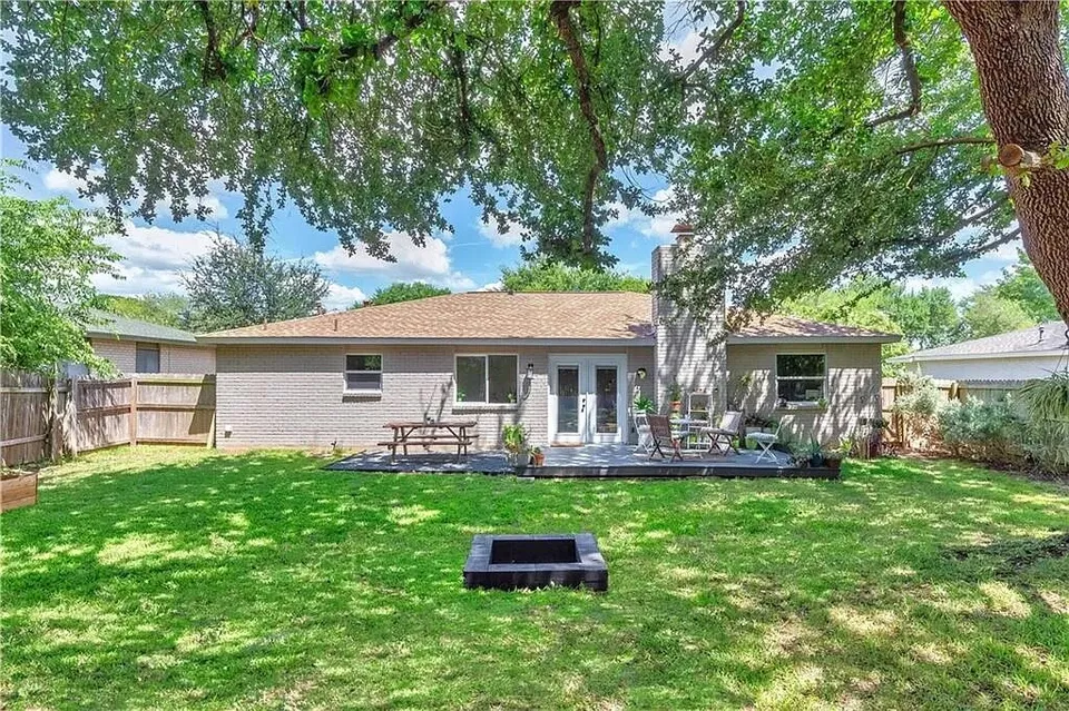Back of the brick ranch house with a deck and a fire pit in a shaded lawn