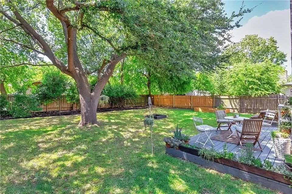 Backyard with a large tree, a garden bed and a deck with chairs