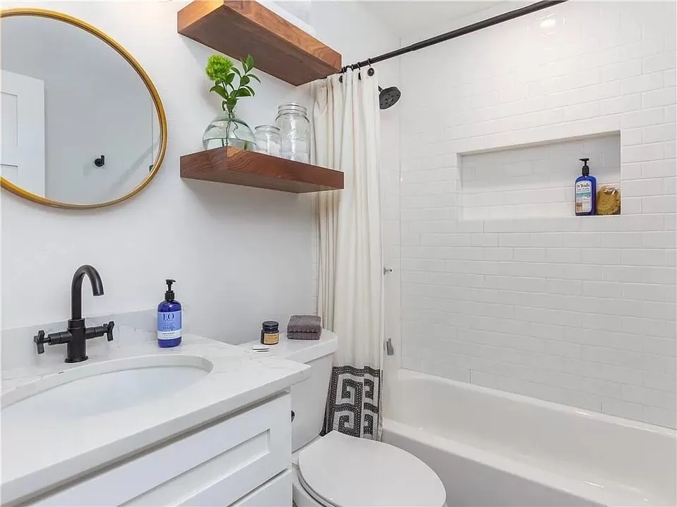 Bathroom with a tub, a round brass mirror and walnut floating shelves