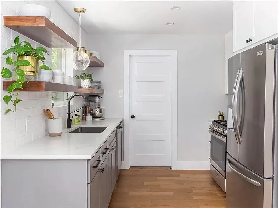 Galley kitchen with walnut floating shelves, a stainless refrigerator and a white door