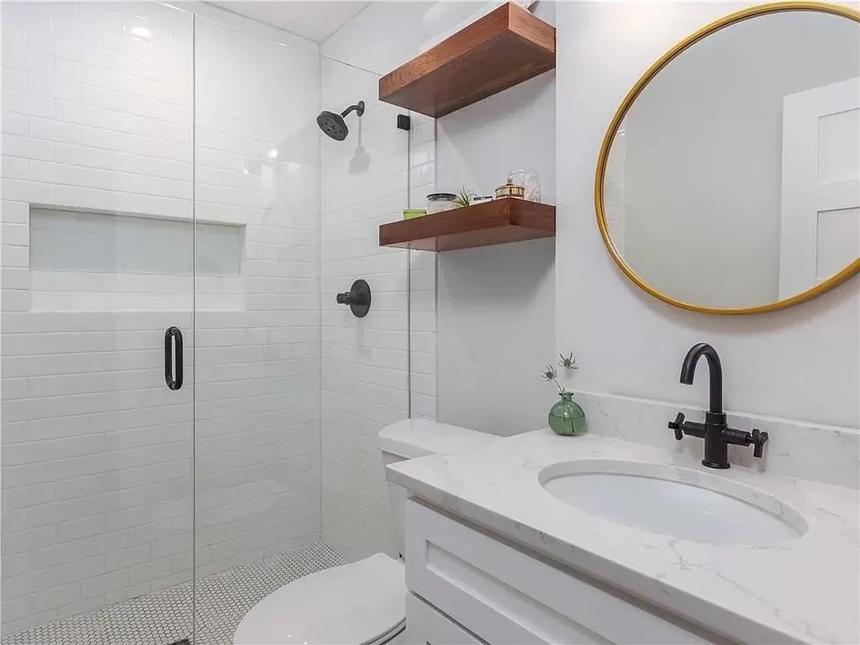 Glass shower with white subway tile, walnut shelves and a round brass mirror