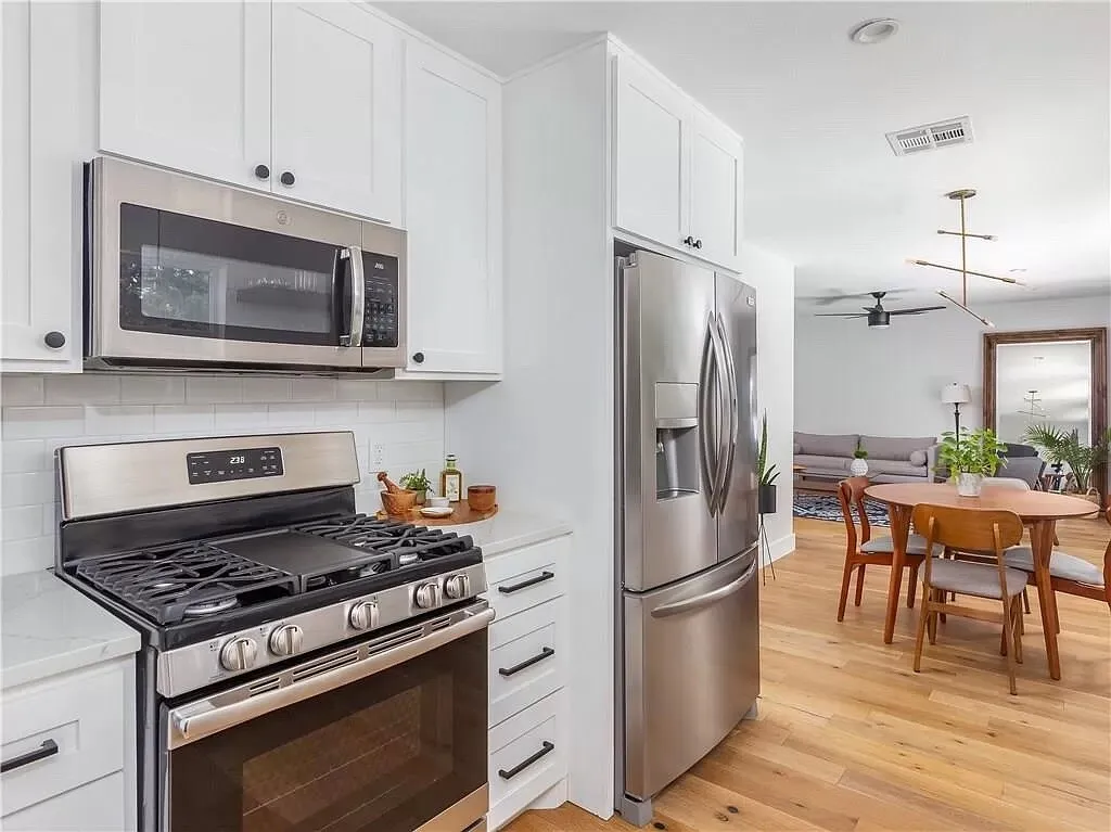 White kitchen with a gas range, a stainless refrigerator and microwave, open to a round dining table
