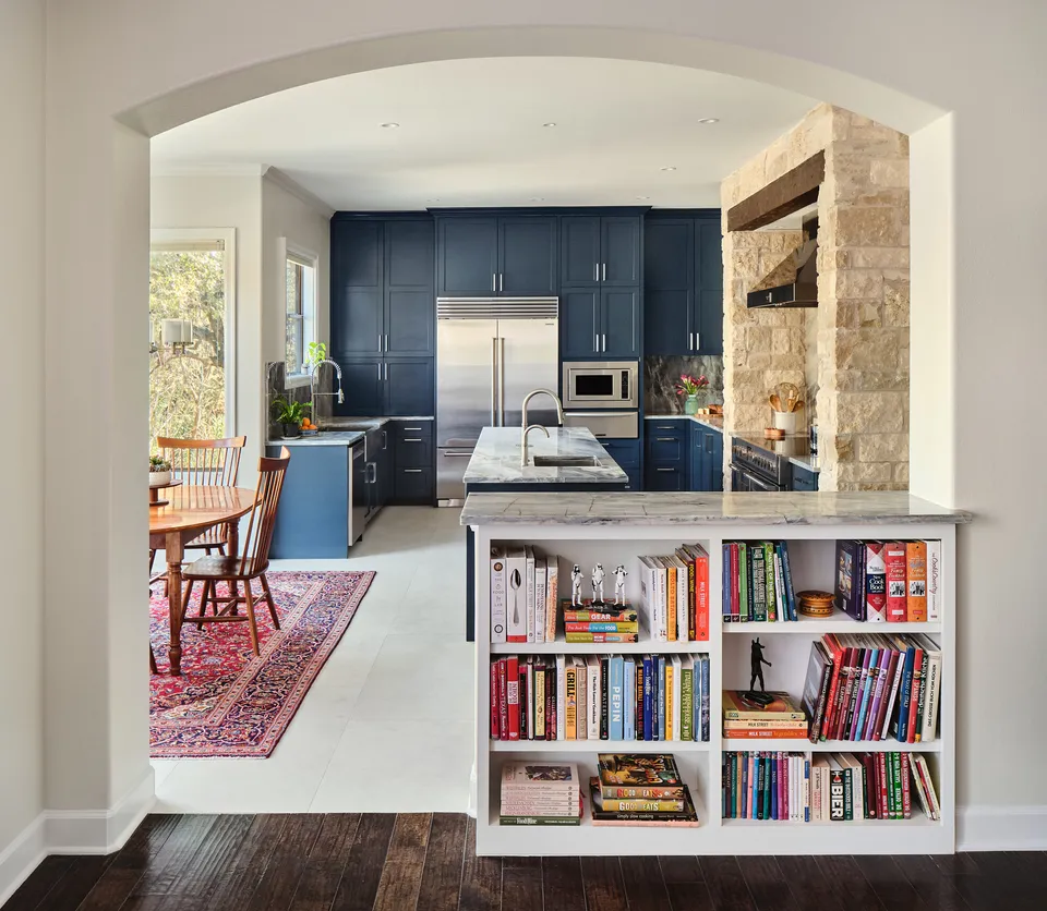 Arched opening with a built-in bookshelf looking into the navy kitchen