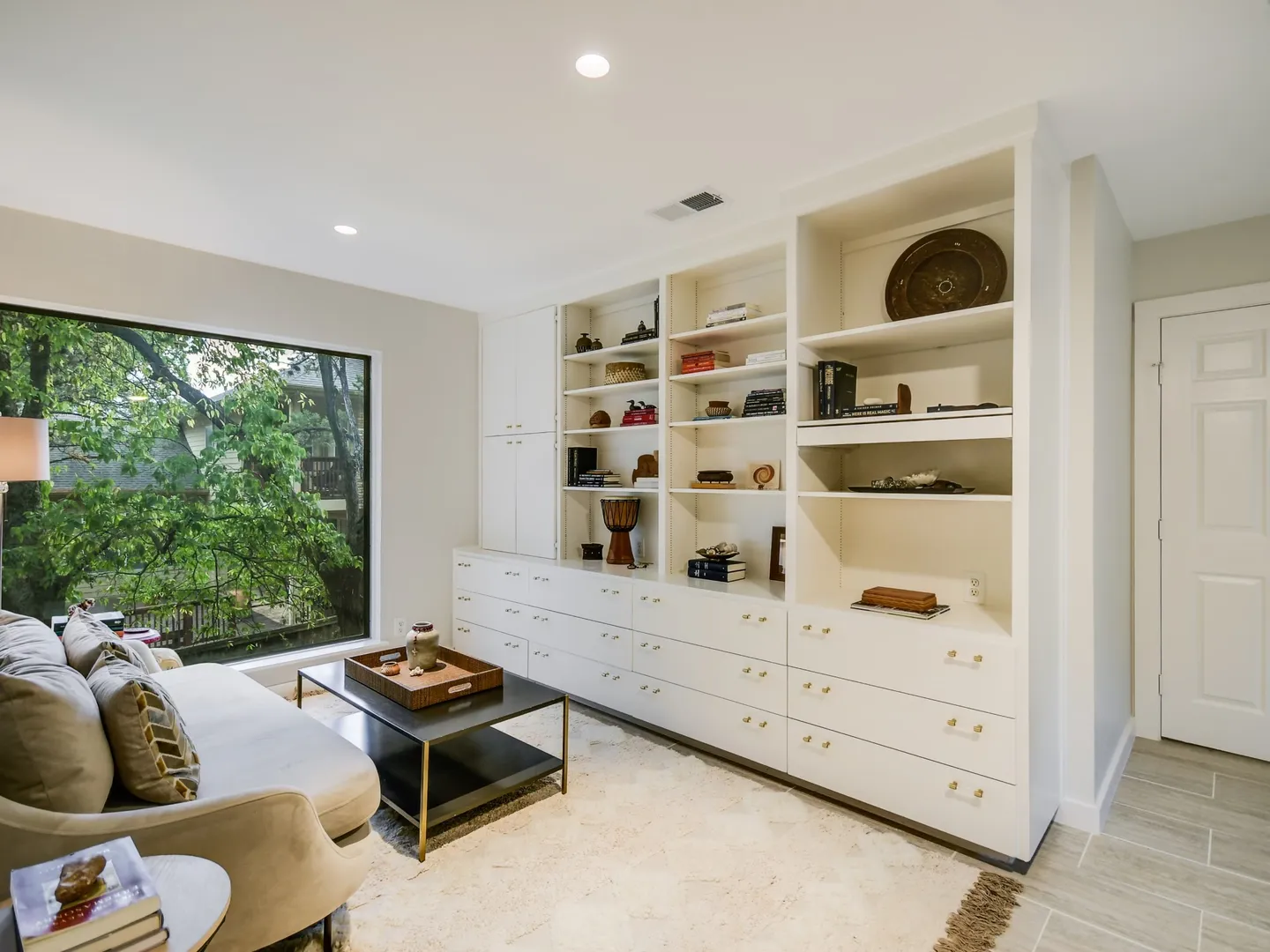 Sitting room with white built-in shelving and a large window onto trees
