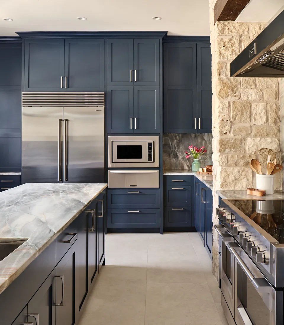 Navy cabinets with a built-in stainless refrigerator and microwave beside the limestone range wall