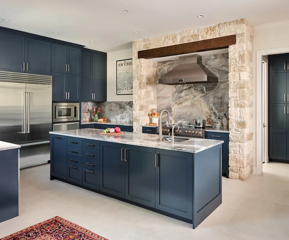 Navy kitchen island facing the limestone range alcove with a wood beam