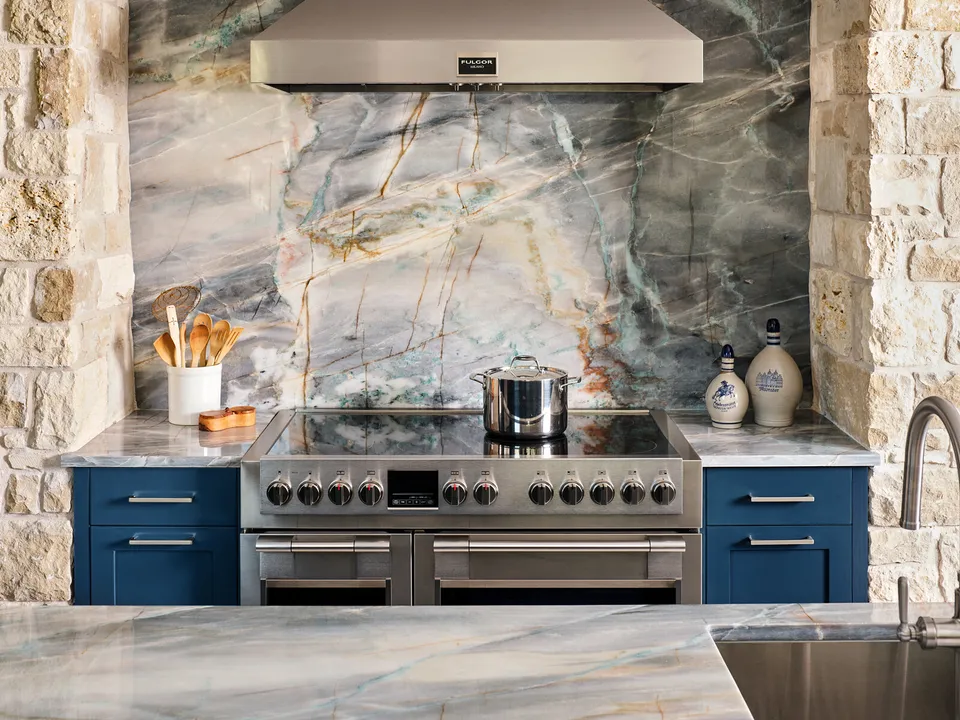 Range with a stainless hood in a limestone surround and a quartzite backsplash slab