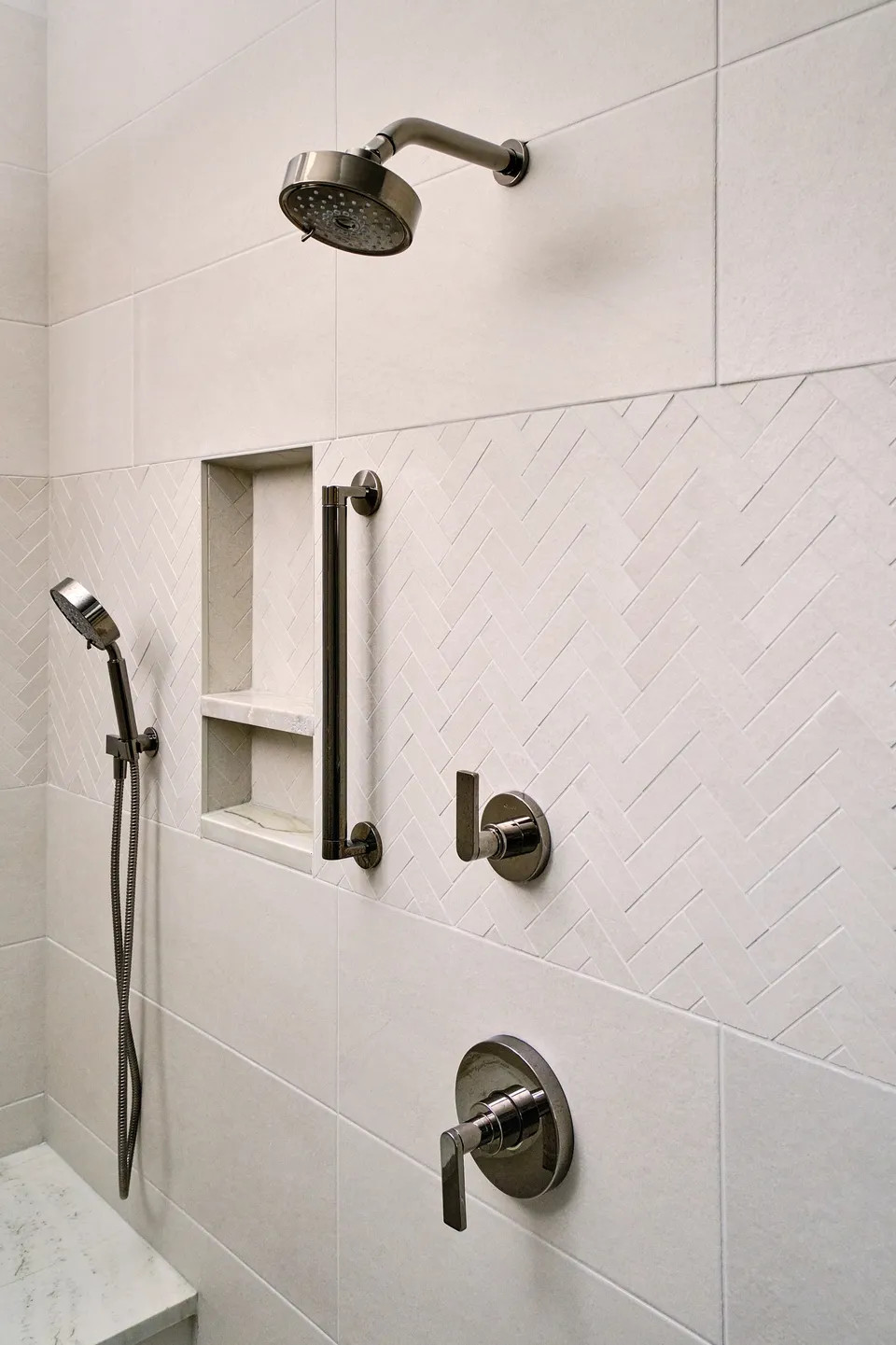 Shower with large white tile, a herringbone accent wall, a niche and a grab bar
