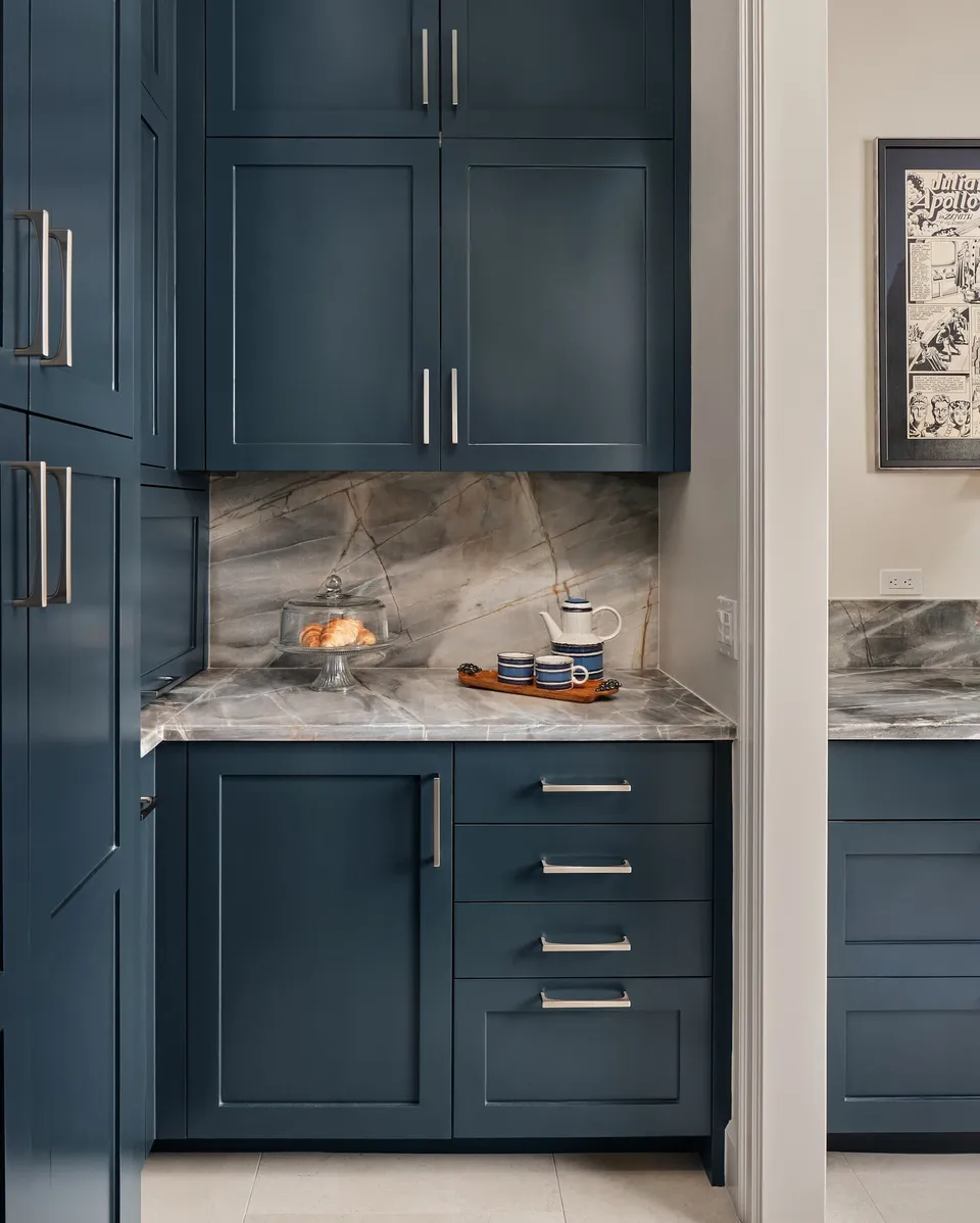 Tall navy pantry cabinets beside a quartzite backsplash