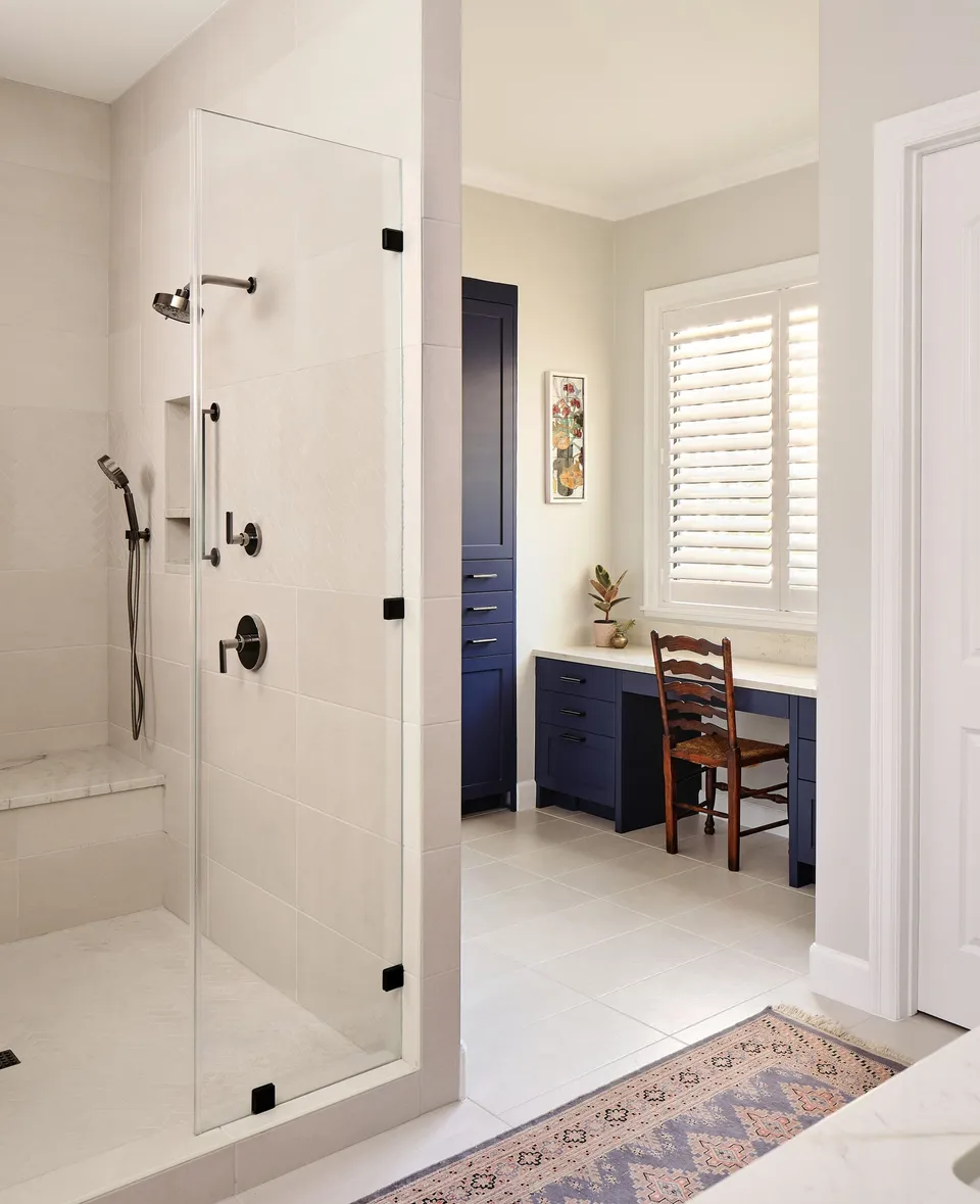 Walk-in shower with a frameless glass door beside a navy built-in desk