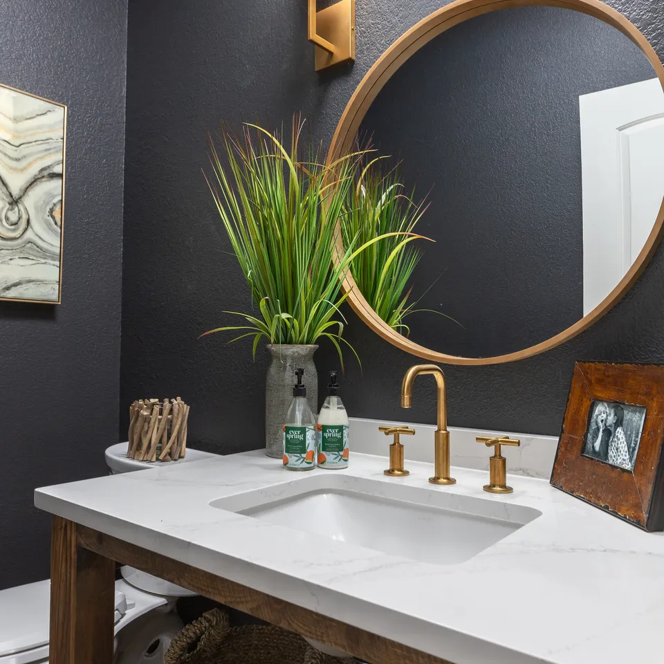 Powder bath with a charcoal wall, a round brass mirror and a wood vanity