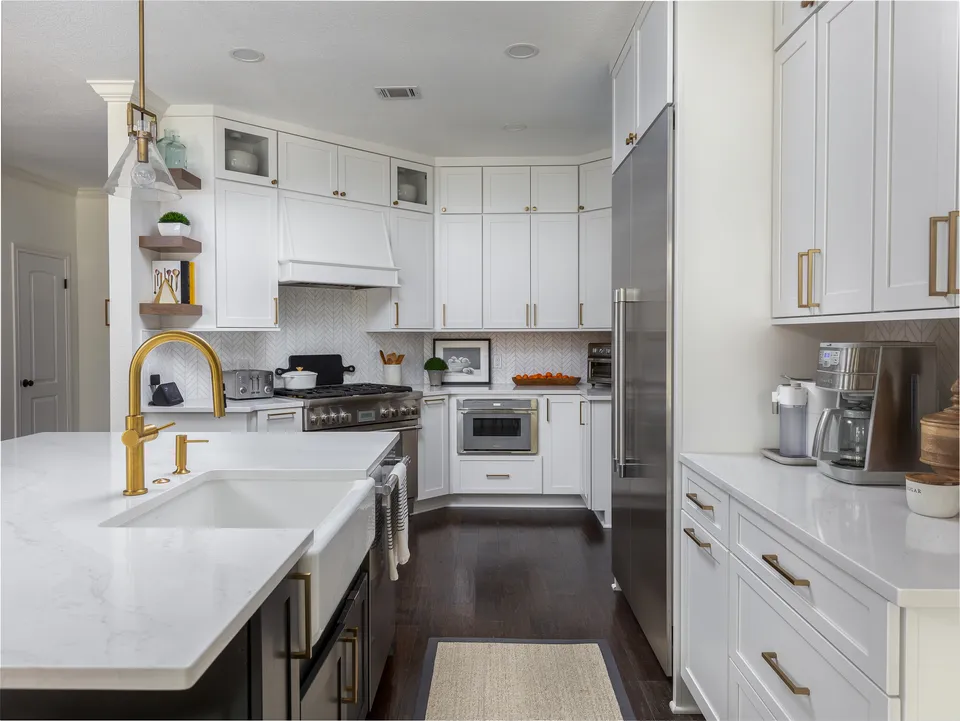 White kitchen with a large island, a brass faucet and a farmhouse sink