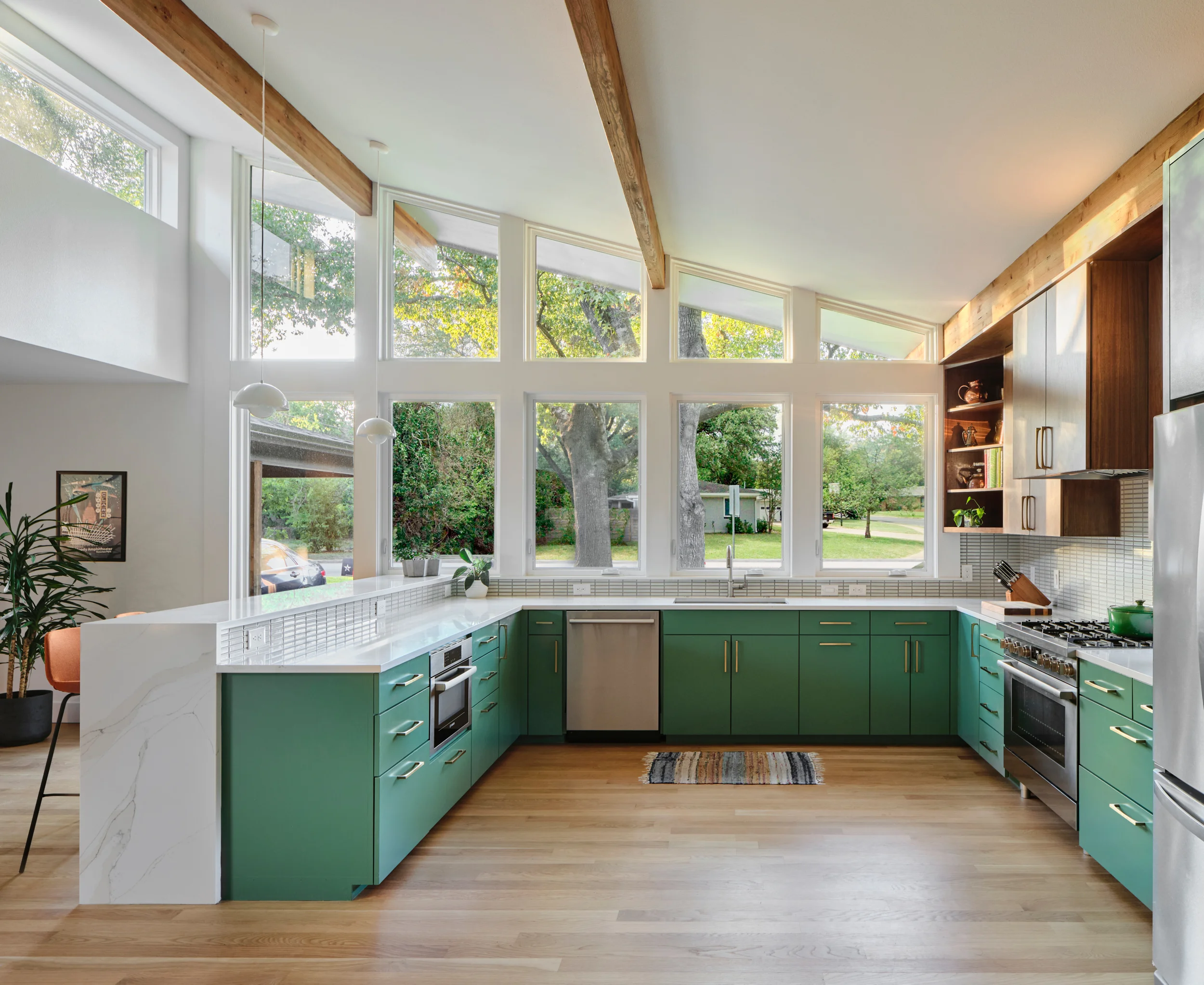 Kitchen with green cabinets under a wall of tall windows and clerestory windows below exposed wood beams