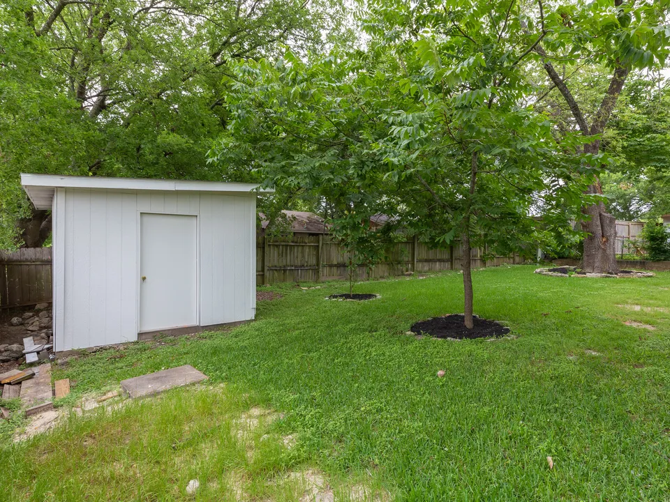 Backyard with a white storage shed and young trees
