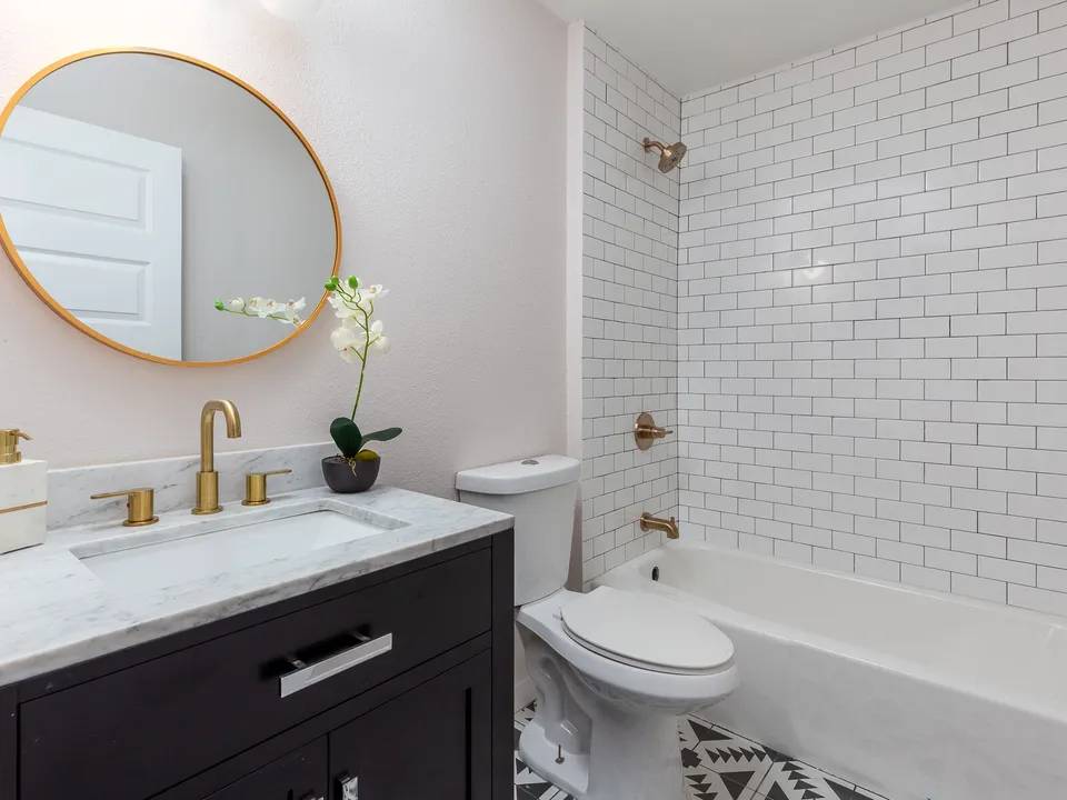 Bathroom with a black vanity, a round brass mirror and a subway tile tub surround