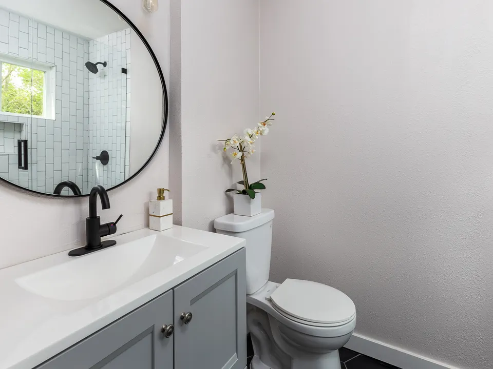 Bathroom with a grey vanity, a round black mirror and a tiled shower