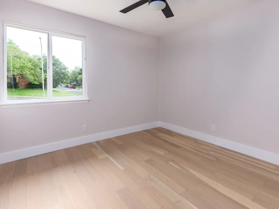 Empty bedroom with a large window and light oak floors