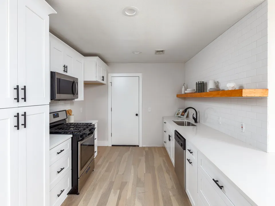 Galley kitchen with white cabinets, a gas range and a walnut shelf