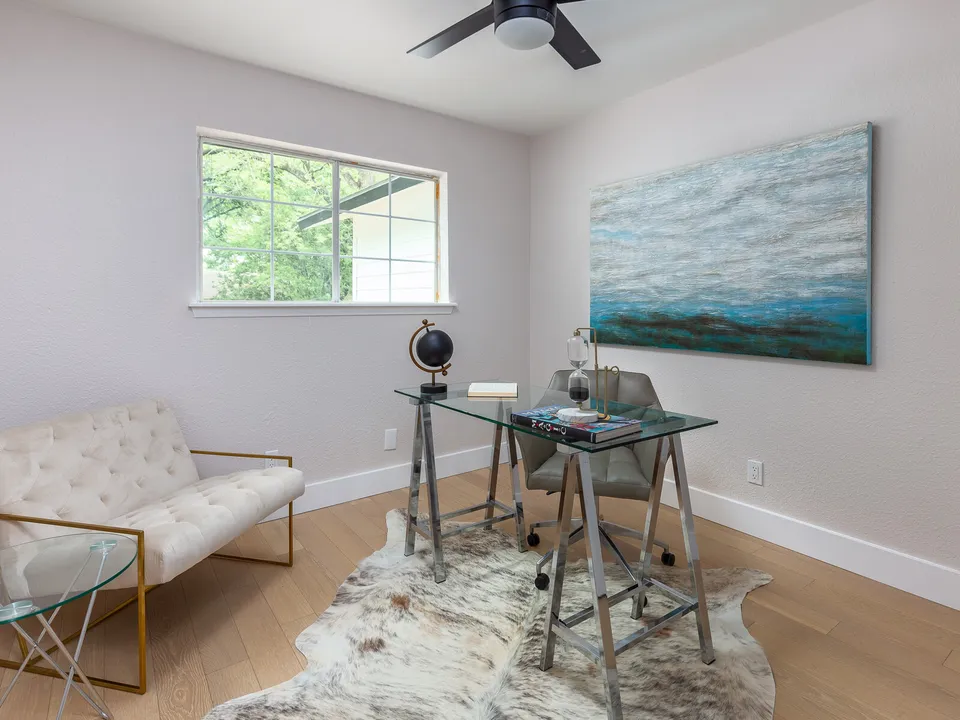 Room with a glass desk, a tufted settee and a large blue painting