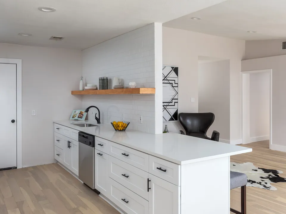 White shaker kitchen with a walnut floating shelf and a peninsula