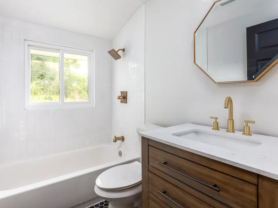 Bathroom with a wood vanity, a gold octagon mirror and a tub