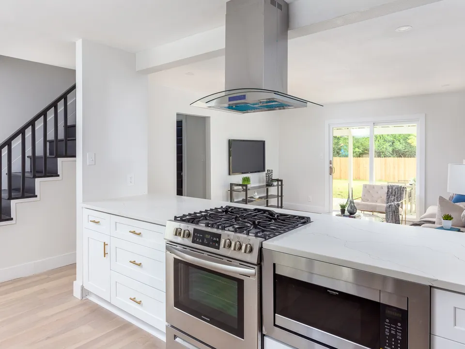 Gas range and chimney hood on a white peninsula beside the stairs