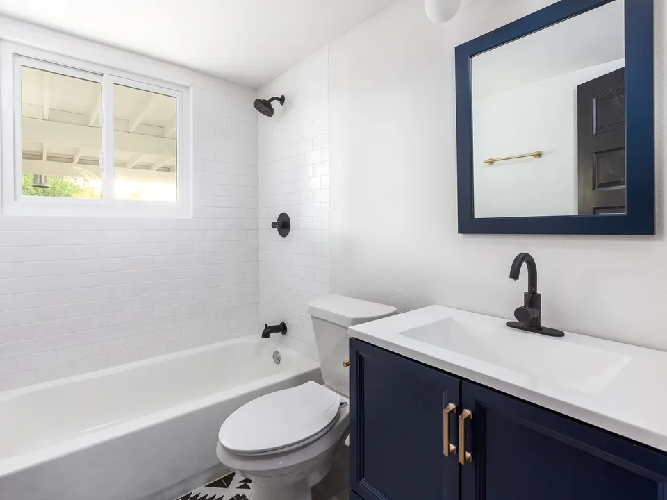 Hall bath with white tile, a navy vanity and brass hardware