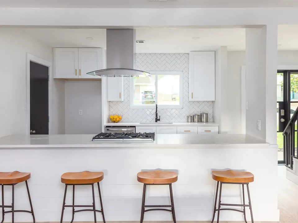 Kitchen peninsula with four wood bar stools and a chimney hood beyond