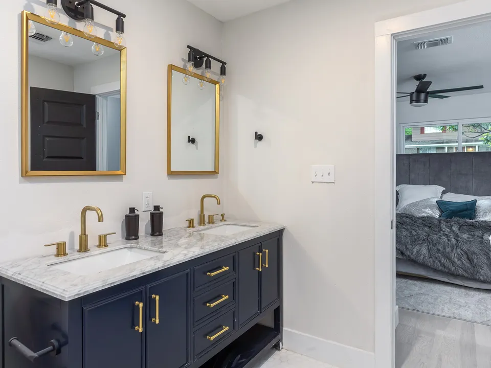 Navy double vanity with brass fixtures and gold mirrors, open to the bedroom