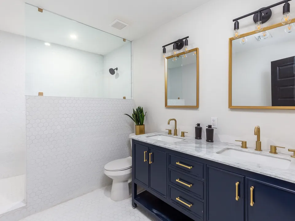Primary bath with a navy double vanity, gold mirrors and a glass shower
