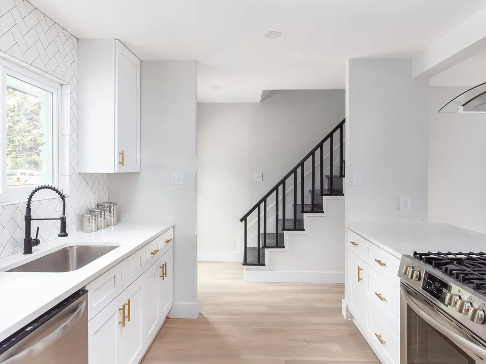 Sink with a black faucet, white herringbone tile and the stairs beyond