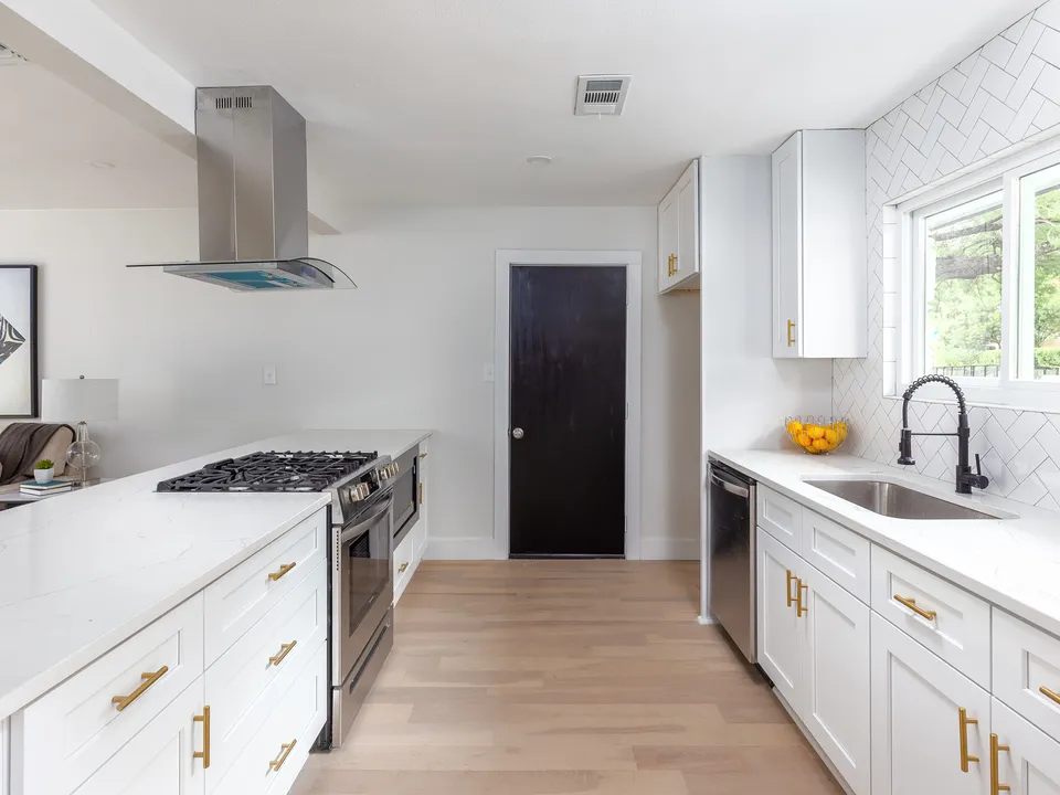 White kitchen with a glass chimney hood, brass pulls and a black door