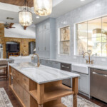 Traditional style kitchen with grey shaker cabinets, stainless Steel appliances, white hand made square tiled backsplash. The focal point of the kitchen is the white oak stained island that stretches across the kitchen, complete with natural stone countertop